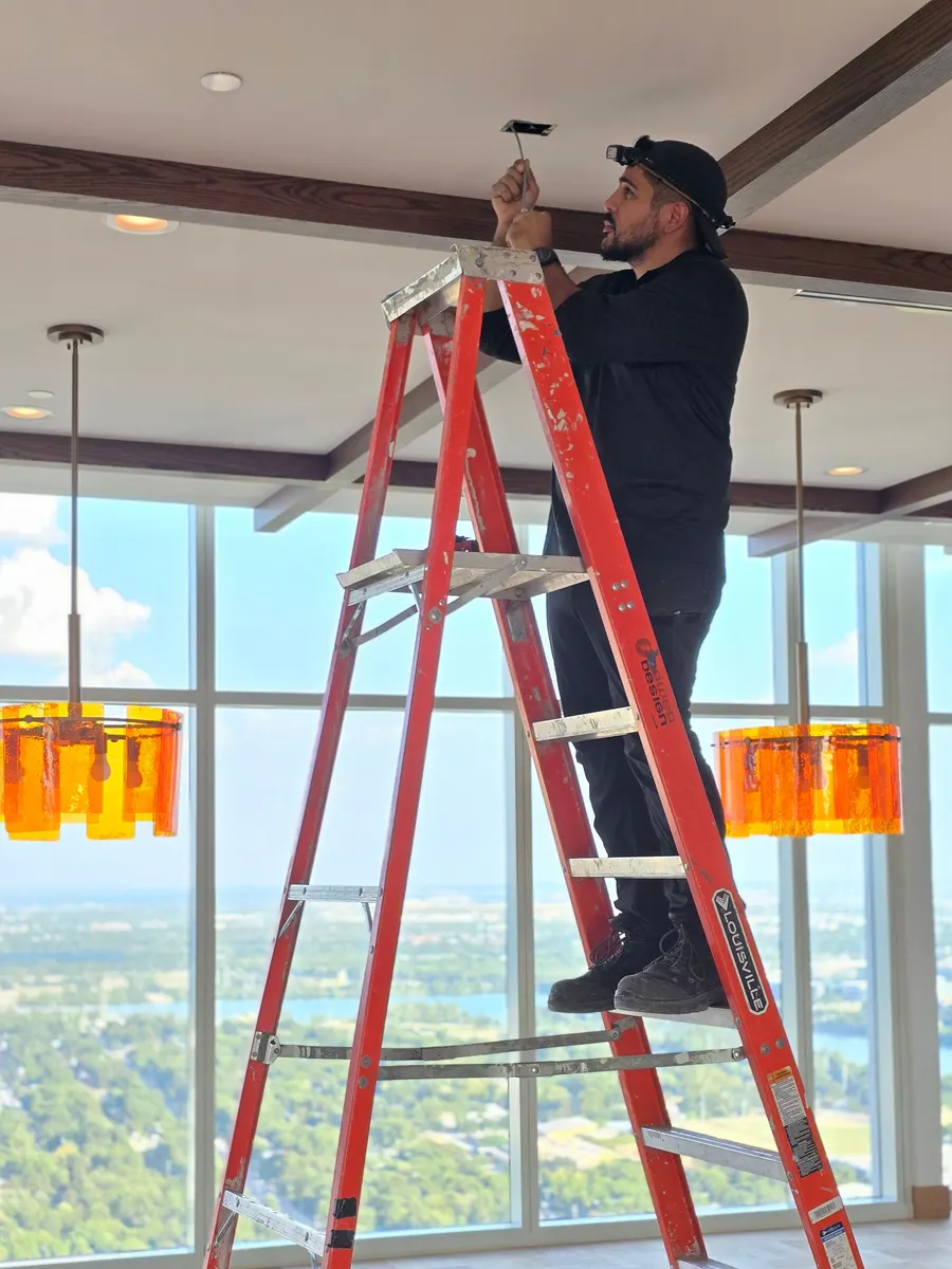 Joshua on a ladder installing ceiling hardware in a high-rise space