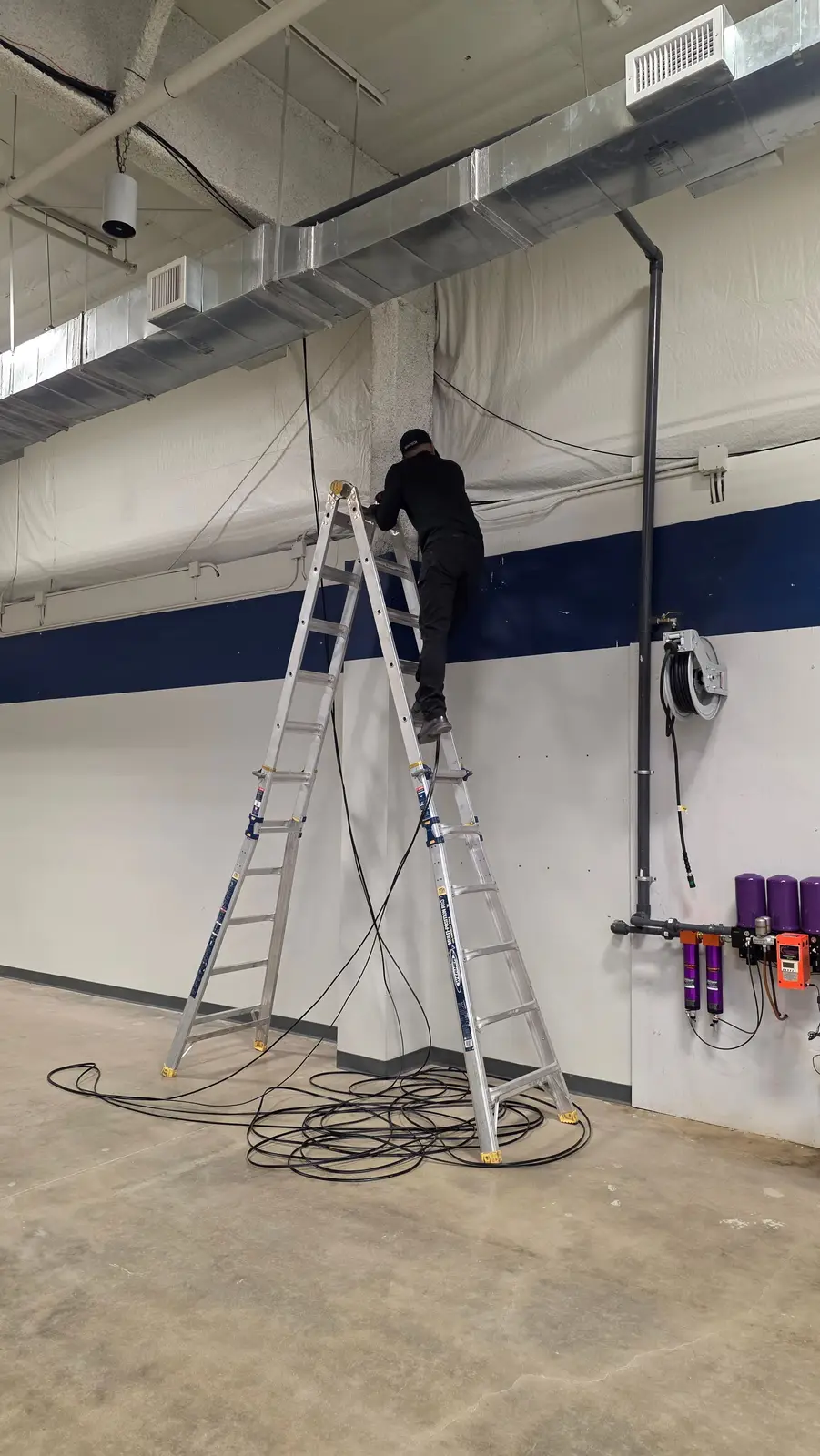 Technician on a tall ladder running cable along a shop wall