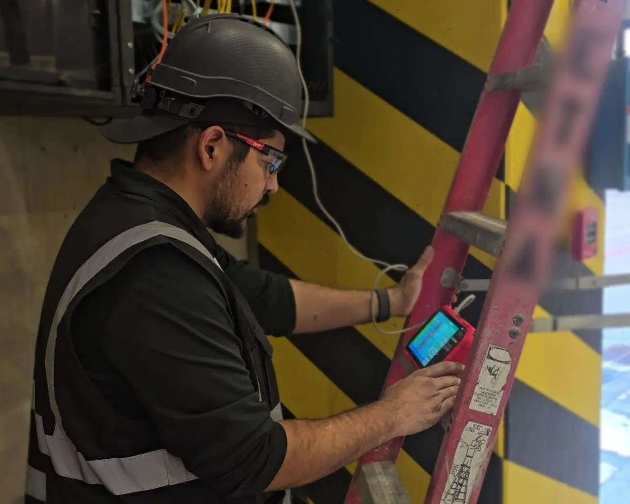 Joshua in a hard hat and safety glasses testing cabling with a handheld tester