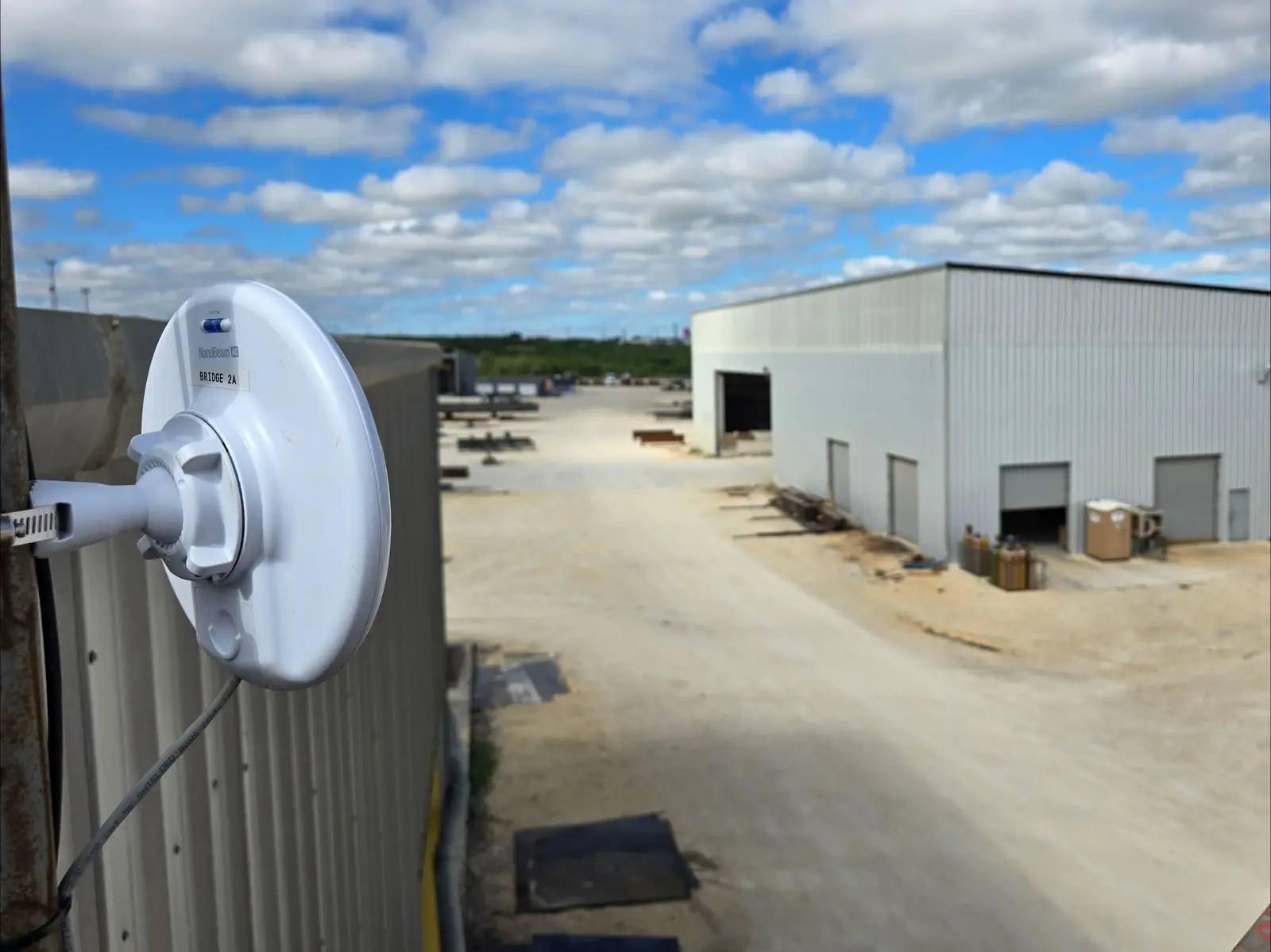 Wireless bridge dish aimed across a yard toward a detached metal building