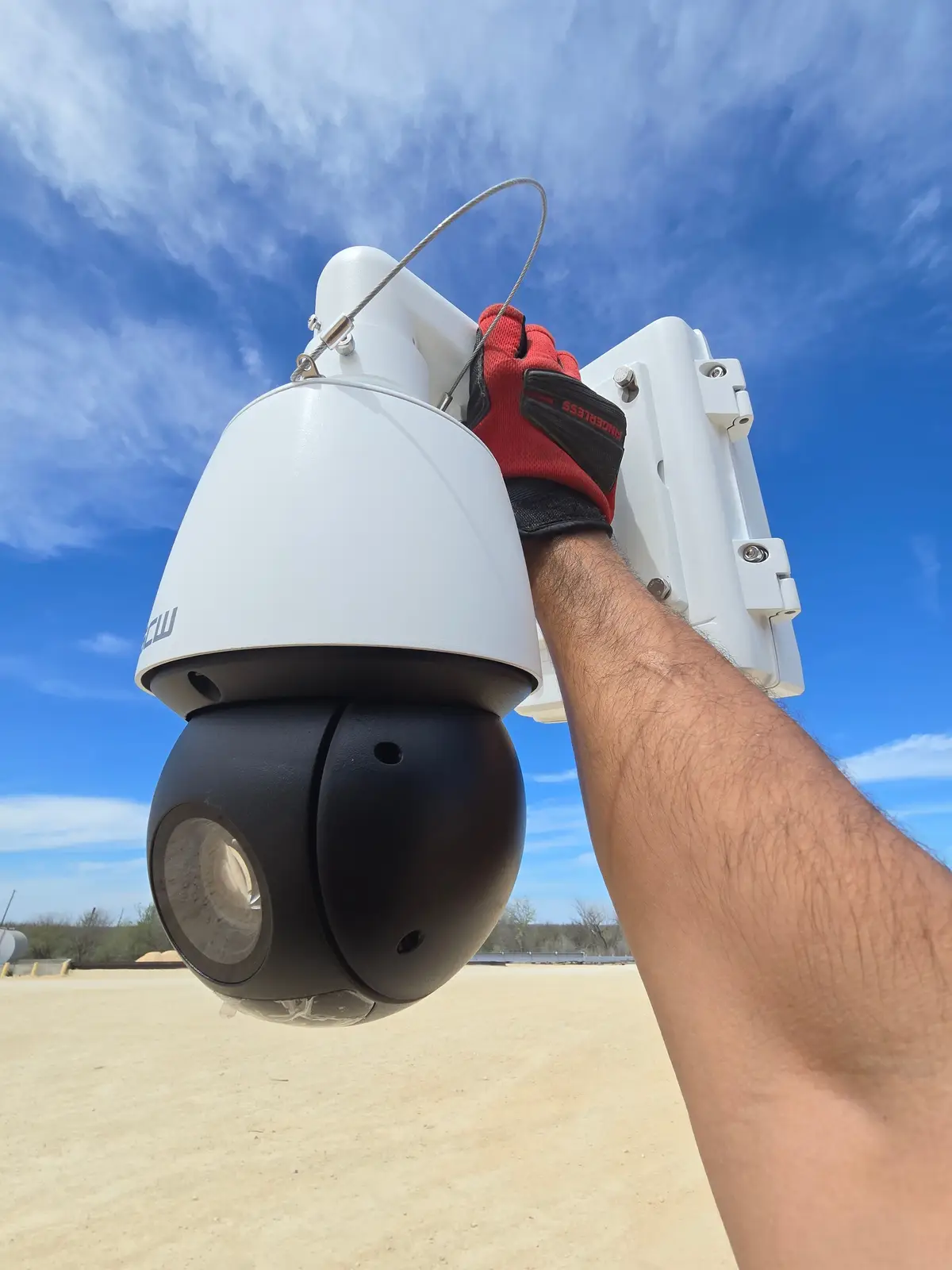 Hand holding a PTZ camera and mount against a blue sky